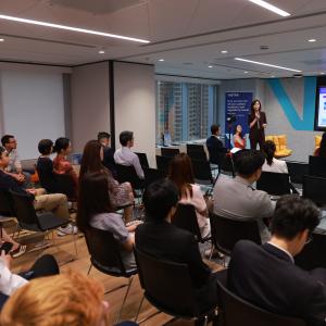 A presenter discusses business insights in a modern conference room, while an audience attentively listens to the presentation.