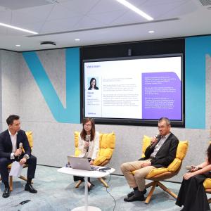 Four people seated on yellow chairs participate in a panel discussion. The room has a modern design, a Vistra banner, and a screen displaying text.
