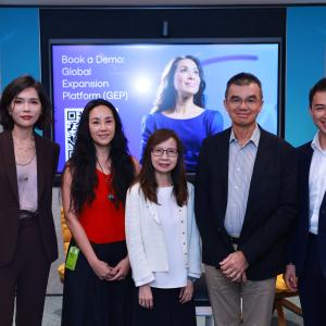 Five people pose confidently in business attire in front of a screen displaying "Book a Demo: Global Expansion Platform (GEP)." The atmosphere is professional and welcoming.